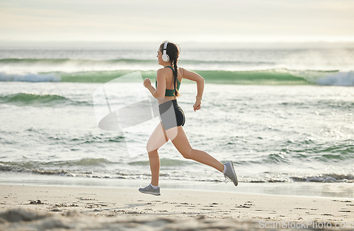 Image of Woman running on beach, listening to music and morning cardio routine for healthy lifestyle in California. Fitness workout by sea, young athlete with headphones and sports exercise in summer