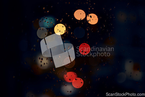 Image of Bokeh, night and lights on a window with water drops, liquid or moisture against a dark abstract background. Blurred light, colorful and rain drop or splash on glass for city view during rainy season