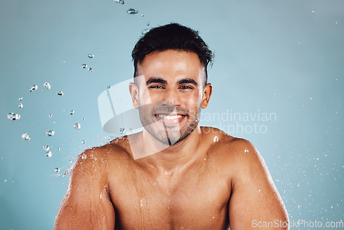 Image of Water drops, portrait and skincare man isolated on blue background face cleaning, body shower and smile. Strong, beauty model or person facial glow in studio headshot washing and dermatology hygiene