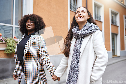 Image of Woman, friends and holding hands walking in the city for friendship, travel or fun journey in the outdoors. Happy women taking walk or stroll touching hand with smile for sightseeing in an urban town