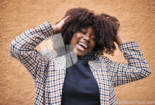 Image of Black woman, laughing and afro for fashion, style or hair against a wall background. Portrait of happy African American female model touching stylish curls and smiling in happiness for haircare