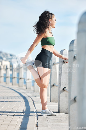 Image of Fitness, woman and stretching legs for running, exercise or cardio workout by the beach in Cape Town. Active female runner in warm up leg stretch preparation for run, exercising or training in nature