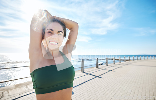 Image of Portrait, stretching and happy fitness by woman at beach for running, exercise or cardio on blue sky background. Face, stretch or workout by girl at ocean training, smile or relax, warm up or routine