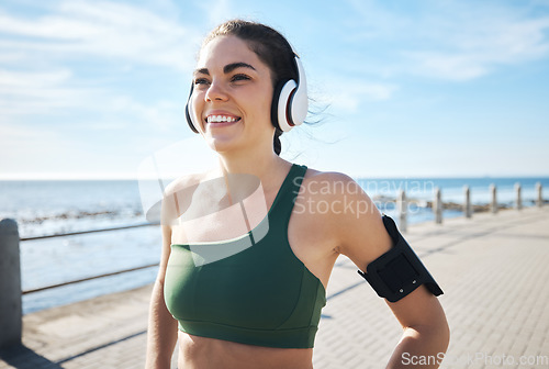 Image of Happy, fitness and woman with music at beach for running, exercise and cardio on blue sky background. Radio, podcast and workout run by girl at ocean for training, smile or relax in audio motivation