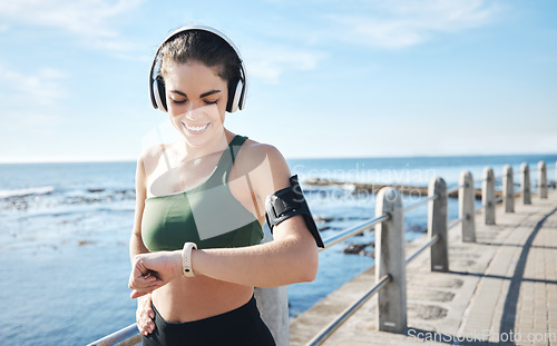 Image of Headphones, smartwatch and woman running for workout, exercise and health results, progress or fitness steps. Goals, check timer and sports person at beach listening to music or podcast for training