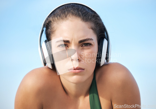 Image of Headphones, fitness and portrait of woman in focus, mindset and goals of podcast or music for motivation. Challenge, power and athlete or sports person face listening to audio technology on blue sky