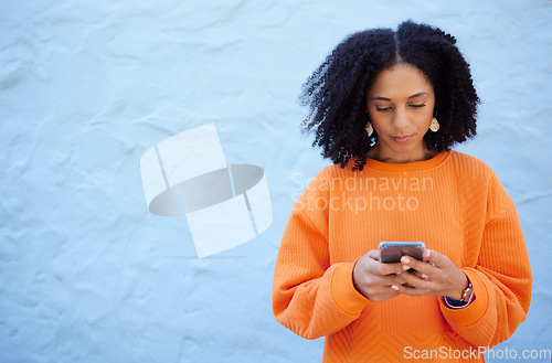 Image of Black woman, cellphone and typing on blue background, wall or mockup. Female with mobile, technology and social media for reading notification, online advertising and website contact on 5g networking