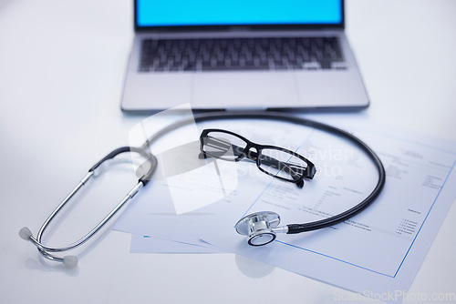 Image of Laptop, stethoscope and medical documents in a office for research, diagnosis or test results. Computer, technology and glasses on a desk for doctor to read healthcare paperwork in hospital or clinic