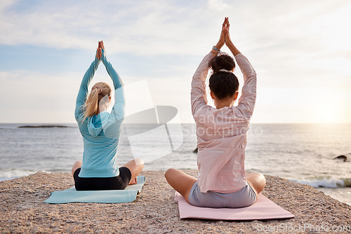 Image of Yoga, back and arms raised on sunrise beach, ocean or sea for morning meditation, chakra balance and bonding. Yogi, women and relax friends on nature rock for zen, healthcare wellness or spirituality