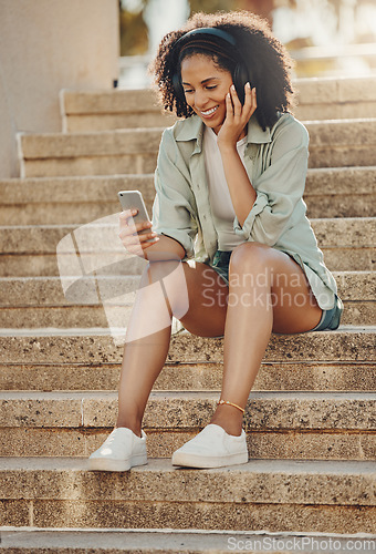 Image of Black woman outdoor, phone and headphone for music, travel and 5g network for audio streaming in city. Happy person in Miami, listen to radio or podcast, relax on steps with internet and urban