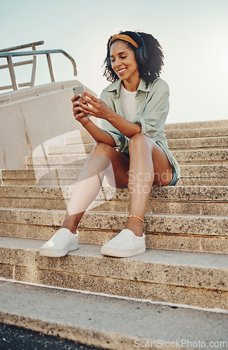 Image of Black woman outdoor, smartphone and headphones for music, travel and 5g network for audio streaming in city. Happy person in Miami, listen to radio or podcast, relax on steps with internet and urban