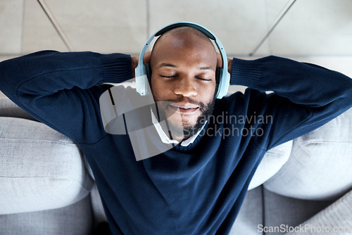 Image of Top view, music headphones and black man on sofa in home living room streaming audio. Meditation, relax technology and male on couch in lounge listening to peaceful podcast, radio or sound in house.