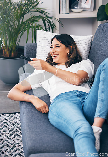 Image of Watching tv, relax and a woman on a sofa in the living room of her home streaming a subscription service. Television, channel surfing and comedy with an attractive young female lying in her lounge