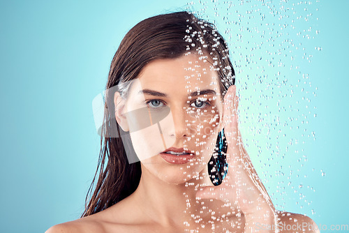 Image of Face, water splash and skincare of woman in shower in studio isolated on a blue background. Beauty, portrait and young female model washing, cleaning or bathing for hygiene, wellness and health.