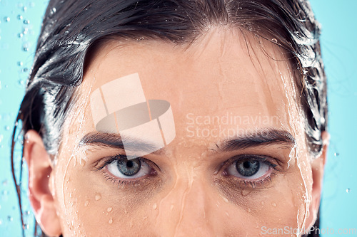 Image of Water splash, skincare and eyes of woman in shower in studio isolated on a blue background. Beauty, face portrait and young female model washing, cleaning or bathing for hygiene, wellness and health.