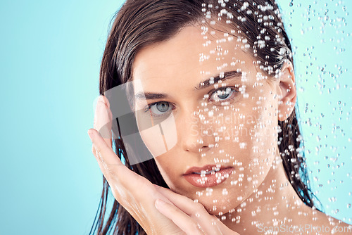 Image of Water splash, face and skincare of woman in shower in studio isolated on a blue background. Beauty, portrait and young female model washing, cleaning and bathing for hygiene, wellness and health.