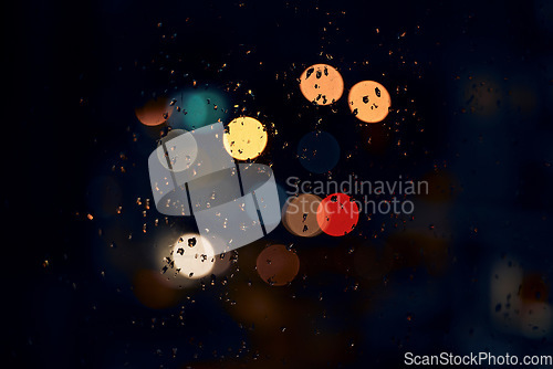 Image of Night, bokeh and lights on a window with water drops, liquid or moisture against a dark abstract background. Blurred light, colorful and rain drop or splash on glass for city view during rainy season