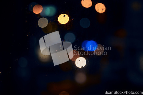 Image of Bokeh, night and light on a window with water drops, liquid or moisture against a dark abstract background. Blurred lights, colorful and rain drop or splash on glass for city view during rainy season