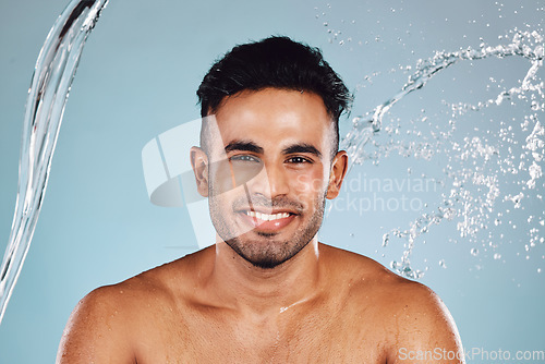 Image of Water splash, portrait and beauty man isolated on blue background face cleaning, body shower and smile. Happy, skincare model or person facial glow in studio headshot washing and dermatology hygiene