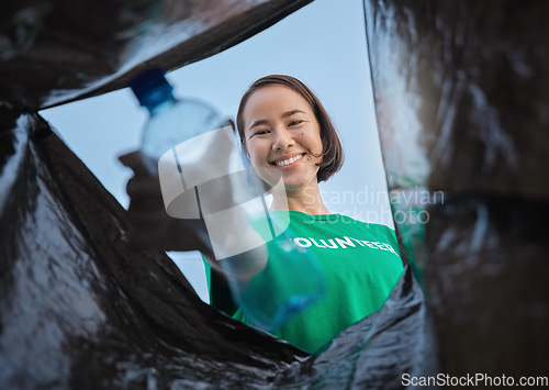 Image of Recycle, bottle and asian woman with view in bag, sustainability and cleaning plastic pollution, earth day and help with community. Saving the environment, charity and people putting trash in garbage