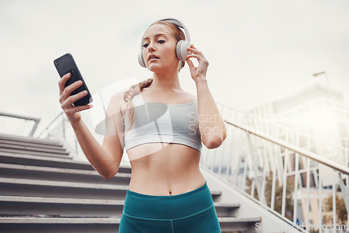 Image of Woman, runner and phone with headphones for music, radio and web texting on chat app by stairs. Gen z girl, urban workout and fitness with smartphone for networking, social media and internet in city