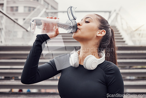 Image of Workout, hydration and a sports woman drinking water outdoor in the city during cardio or endurance exercise. Runner, fitness and hydrated with a female athlete training in an urban town for health