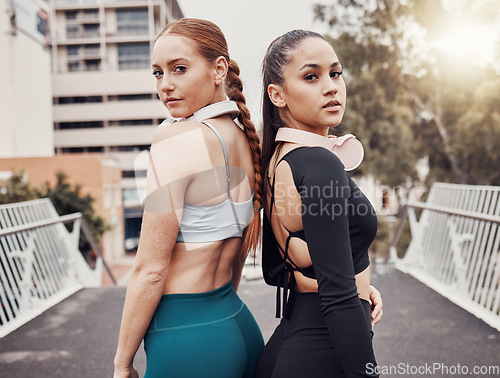 Image of Women, friends portrait and headphones in city for workout, back to back and commitment to self care fitness goal. Woman training group, exercise team and motivation on bridge in metro with support