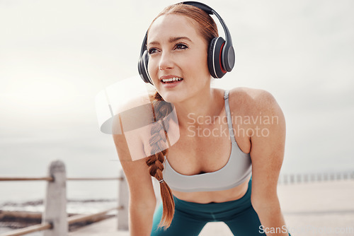 Image of Running, music and face of woman by ocean with motivation, smile and ready for cardio workout. Fitness, sports and happy girl with headphones in Cape Town for exercise, wellness and marathon training