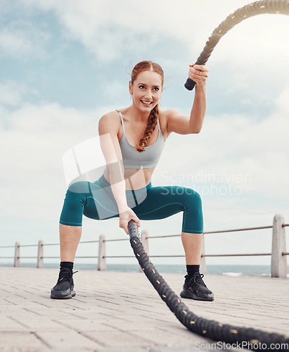 Image of Woman, battle rope exercise and smile at ocean park for fitness, strong body and wellness at outdoor training. Girl, focus and workout by sea with goal, health or motivation for muscle development