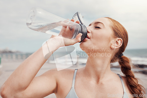 Image of Fitness, woman and drinking water at the beach after running, exercise or cardio workout in Cape Town. Female runner with bottle and natural drink for thirst, hydration or aqua liquid for sport break