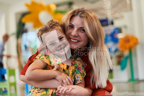 Image of A cute little girl kissing and hugs her mother in preschool