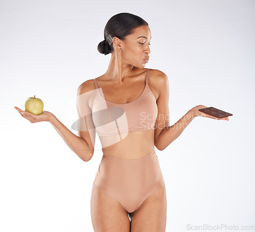 Image of Black woman, studio and choice for chocolate, apple and health for weight loss, body or nutrition by background. Gen z model, underwear or decision for diet, fruit or candy for thinking of cheat day