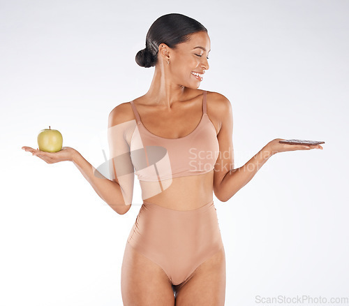 Image of Black woman, fitness and body with an apple, chocolate and smile for balance, wellness and grey studio background. Mockup, African American female and lady with fruit, candy bar and diet on backdrop