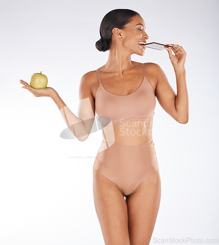 Image of Apple, body and woman eating chocolate in a studio for a sweet snack, candy or craving. Health, wellness and female model enjoying cocoa treat while holding fruit for balance diet by gray background.