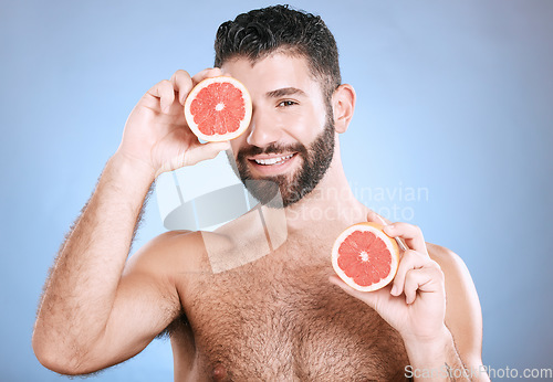 Image of Portrait, beauty and grapefruit with a man model in studio on a blue background for natural skincare or hygiene. Fruit, wellness and nutrition with a handsome male posing to promote a healthy diet