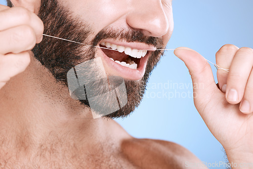 Image of Dental, floss and oral hygiene with a man in studio on a blue background cleaning his teeth for healthy gums. Dentist, healthcare and mouth with a young male flossing to remove plague or gingivitis