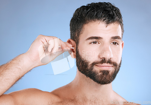 Image of Ear, cleaning and man with cotton bud in studio for hygiene, grooming and beauty routine on blue background. Earwax, product and guy model in cosmetic, luxury and wax, removal or stick while isolated