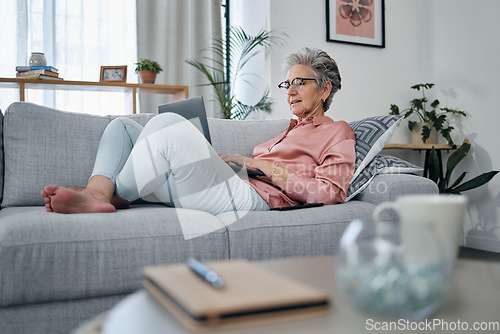 Image of Senior woman, laptop and relax on sofa in the living room checking email, typing or writing at home. Elderly female freelancer or writer relaxing on lounge couch working or reading on computer