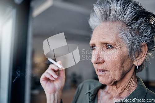 Image of Thinking, nicotine and a senior woman smoking a cigarette in her home while looking out from a window. Idea, smoke and cancer with a mature female tobacco smoker in a house for pension or retirement