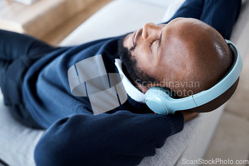 Image of Music top view, headphones and black man on sofa in home living room streaming audio. Meditation, relax technology and male on couch in lounge listening to peaceful podcast, radio or sound in house.