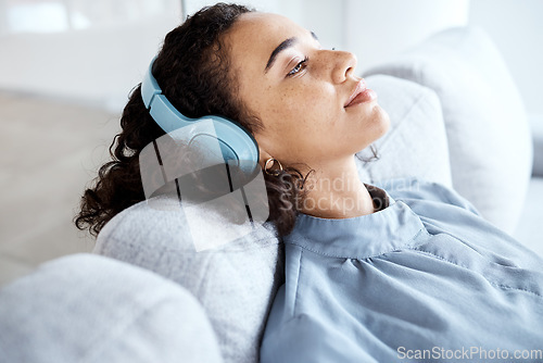 Image of Black woman, headphones and relax on sofa with music, audio streaming and peace with smile in lounge. Young lady, sound technology and listening to radio, podcast and thinking on living room couch