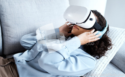 Image of VR, metaverse and gaming with a black woman on a sofa in the living room of her home. AI, 3D and virtual reality with a young female gamer using a headset to access cyberspace for a video game