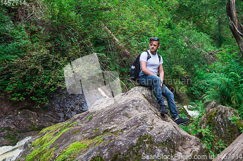 Image of Man traveler with backpack sitting on rock in the forest.