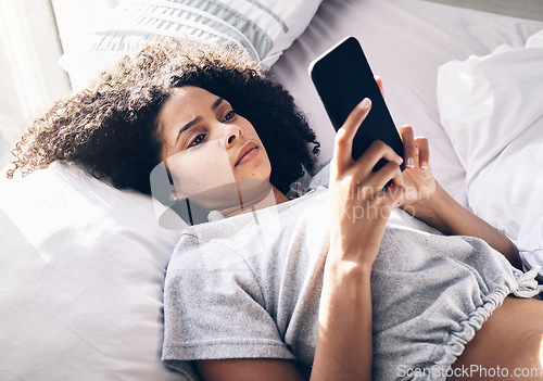 Image of Black woman, sad and typing with phone on bed in home bedroom for social media or internet browsing in the morning. Technology, bored and lonely female with mobile for web scrolling or networking.