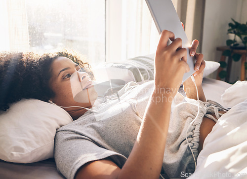 Image of Music earphones, black woman and tablet in bed in bedroom for social media, texting or internet browsing in the morning. Technology, relax and female with touchscreen for streaming podcast or radio.