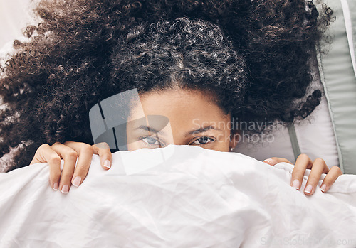 Image of Above bed, portrait and black woman in the morning after sleep rest and relaxing at home with blanket. Eyes, house and wake up happiness of a young person hiding face under the bedroom covers