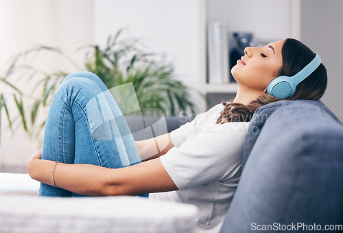 Image of Music, relax and quiet with a woman in her home, listening to the radio while sitting on the living room sofa. Peace, wellness or headphones with an attractive young female streaming audio in a house