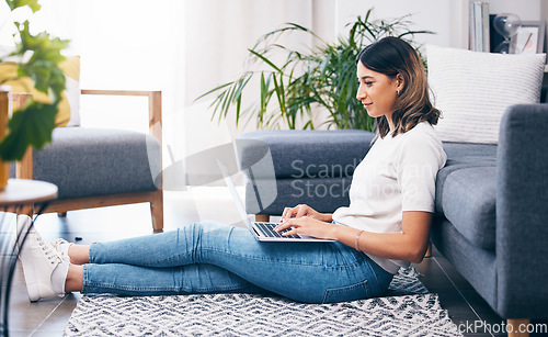 Image of Woman, laptop and typing sitting on floor in the living room by sofa in remote work or studying at home. Female freelancer working on computer checking email, research or browsing in lounge by couch