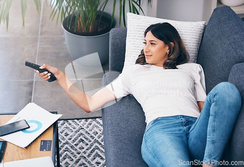 Image of Television, relax and a woman on a sofa in the living room of her home streaming a subscription service. Watching tv, channel surfing and comedy with an attractive young female lying in her lounge