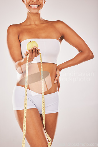 Image of Lose weight, tape measure and body with black woman and apple for nutrition and diet with fitness isolated on studio background. Health, smile and healthy lifestyle with weightloss and clean eating